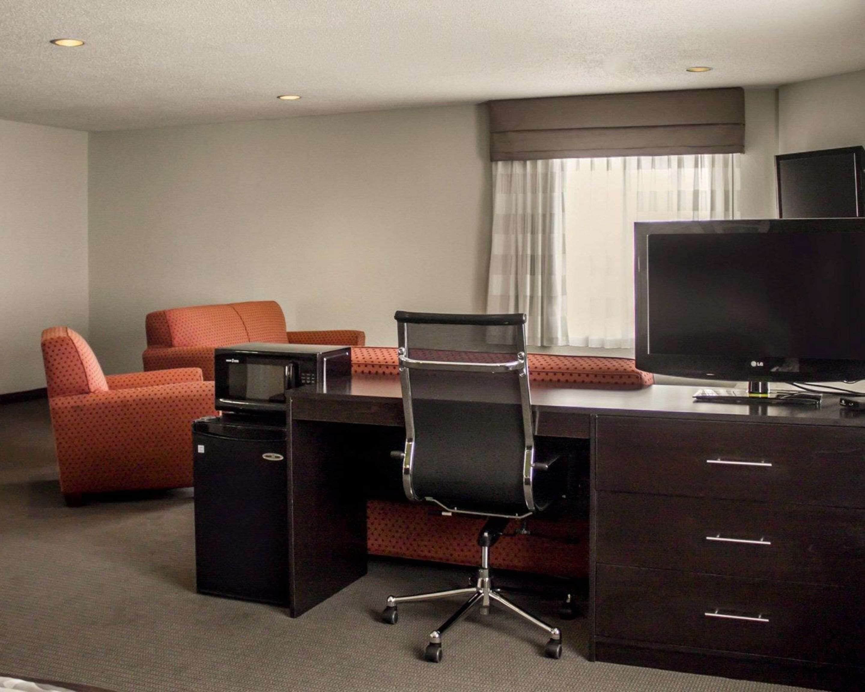 A hotel room with a desk, two orange armchairs, a TV, and a minibar.