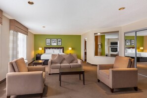 A hotel room with a bed, two armchairs, a coffee table, a nightstand, a lamp, and a mirror. - Sleep Inn Sandusky (Sandusky)