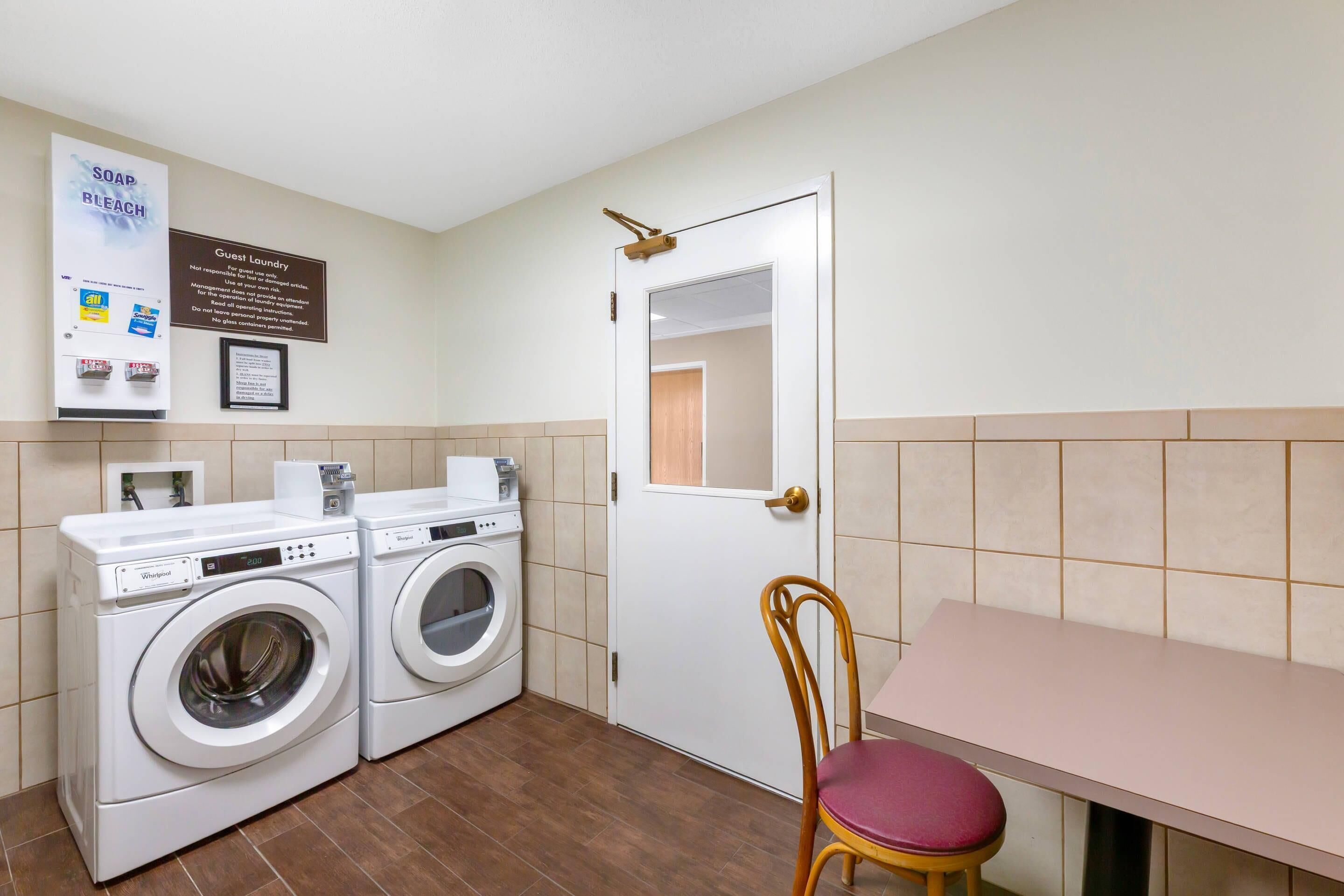 A laundry area with two washing machines, a guest laundry sign, and a table with a chair.