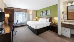 Une chambre d’hôtel comprenant un lit, un bureau, une télévision et une salle de bain avec un miroir et un porte-serviettes.