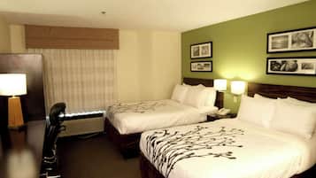 A hotel room with two beds, a desk, and a chair. There are two bedside tables with lamps, a wall-mounted phone, and framed pictures on the wall.