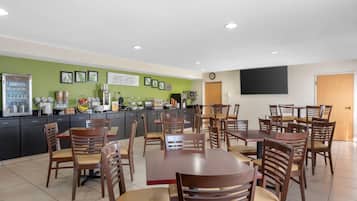 Un restaurante con varias mesas y sillas, una barra con dispensador de bebidas y cuadros en la pared.