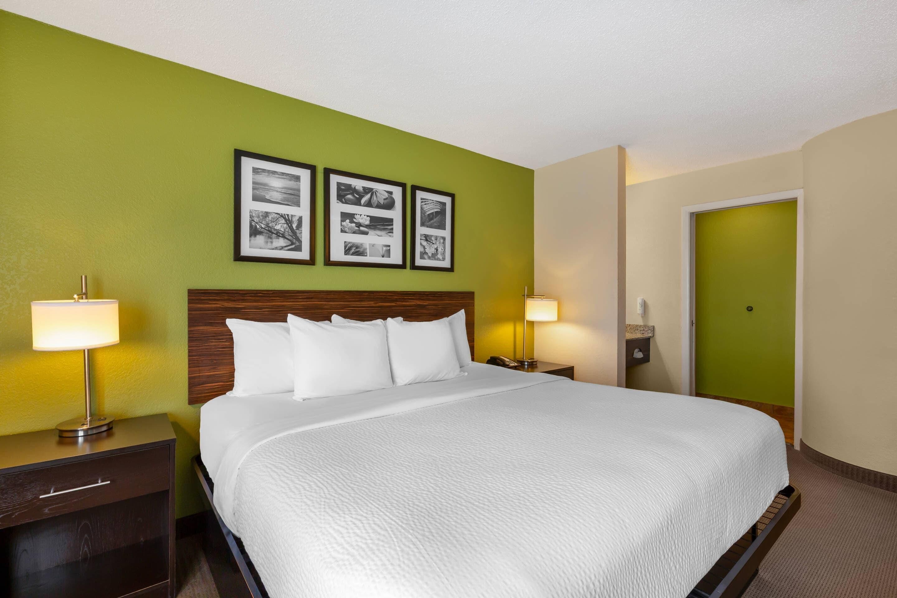 A hotel room with a bed, two bedside lamps, a nightstand, a wooden headboard, and three framed pictures on the wall.
