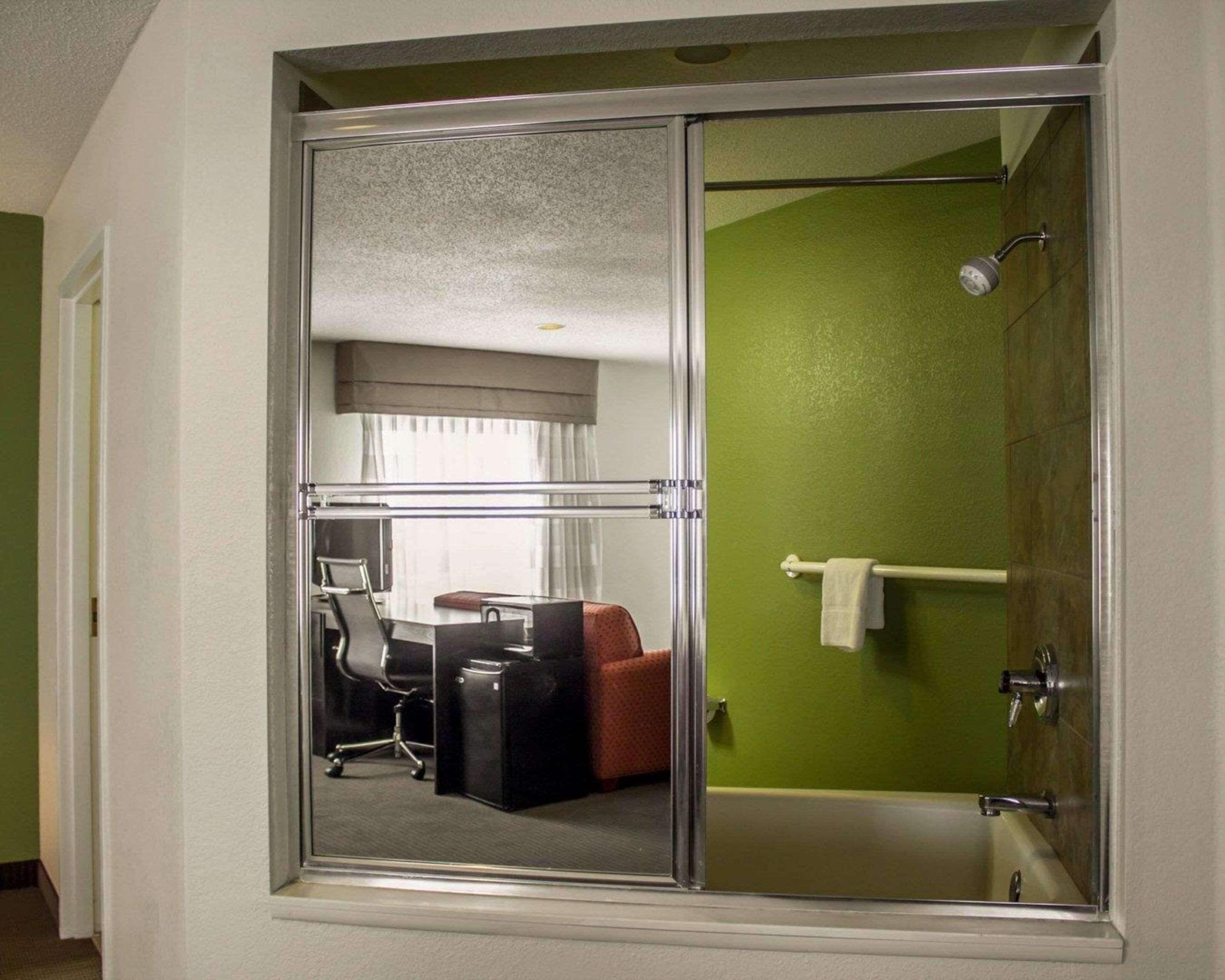 A hotel room with a glass shower enclosure, a bathtub, and a seating area with a desk and chair.