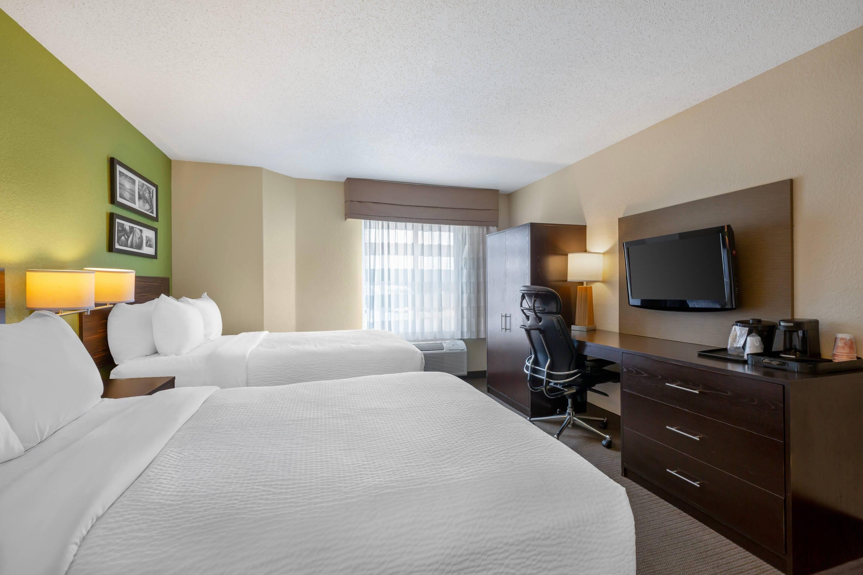 A hotel room with two beds, a desk, a television, and a window with curtains.