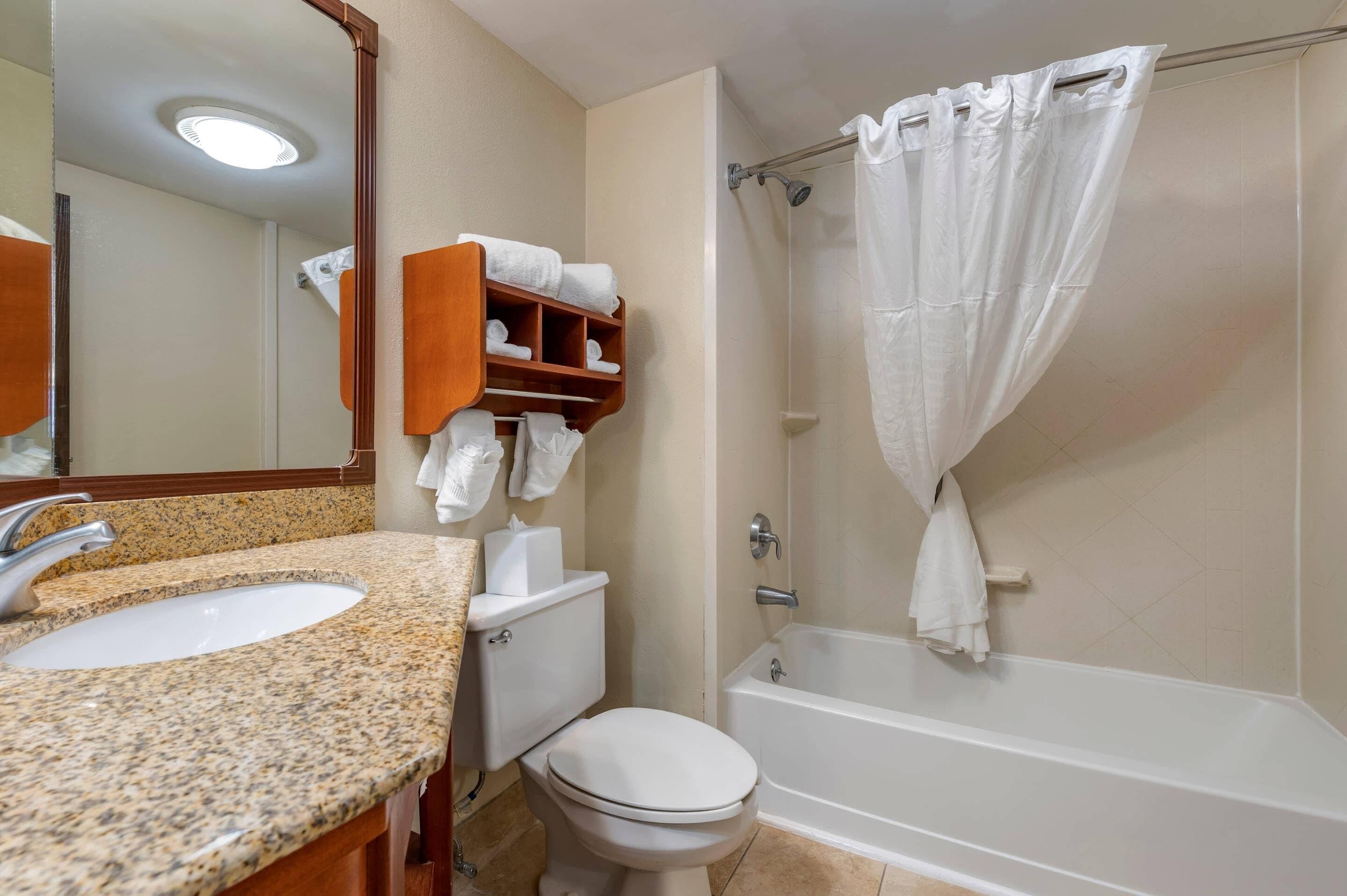 A bathroom with a granite countertop sink, a toilet, a bathtub, and a shower curtain.