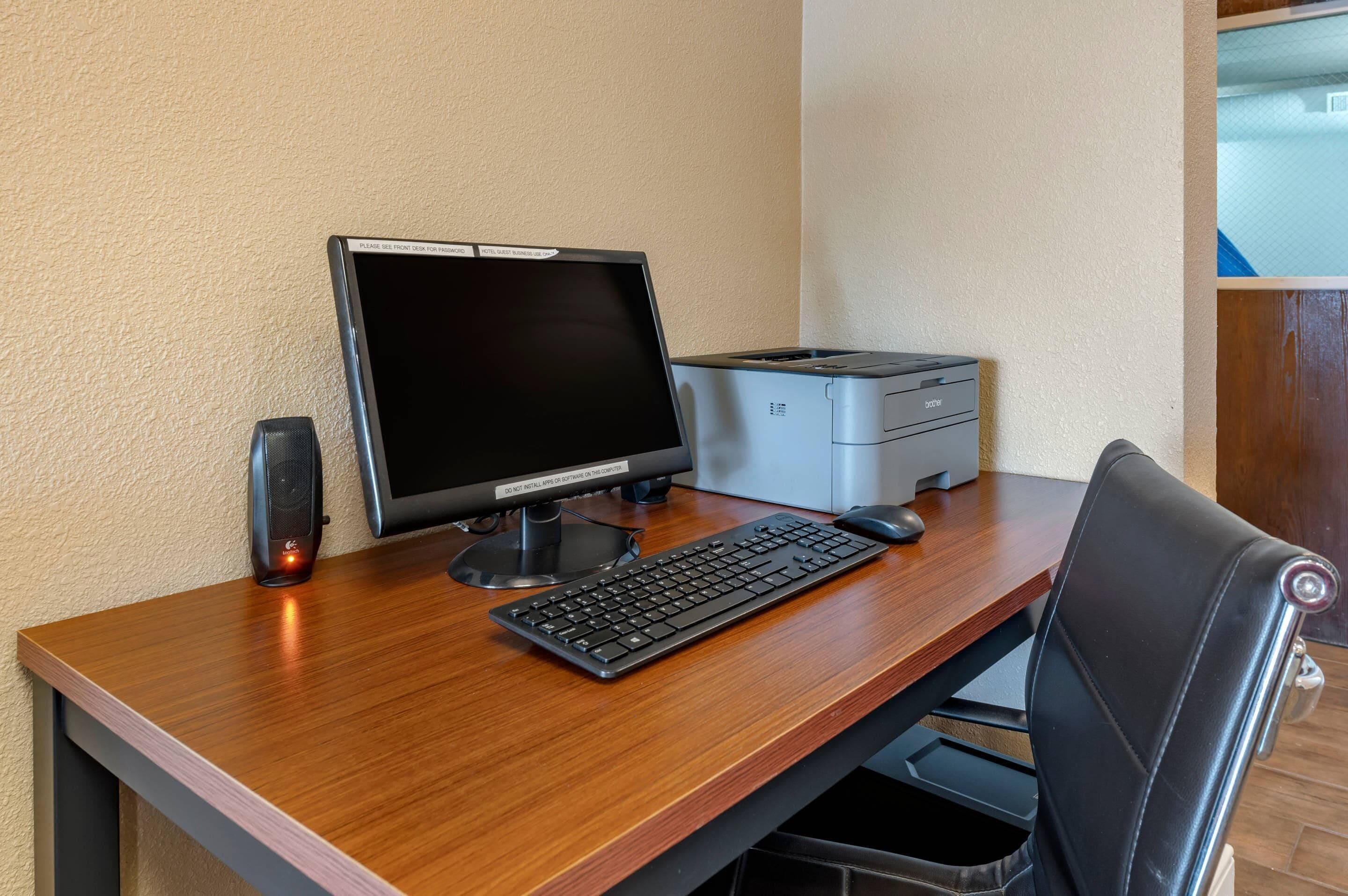 A wooden desk with a black monitor, keyboard, and printer.
