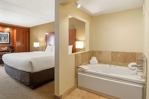 Habitación de hotel con una cama grande, un escritorio con silla, una lámpara de escritorio y un baño con bañera y espejo.