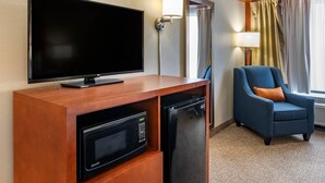 A hotel room with a flat-screen TV, a microwave, a refrigerator, a blue armchair, and a lamp. - Comfort Inn Oxford - University Area (Oxford)