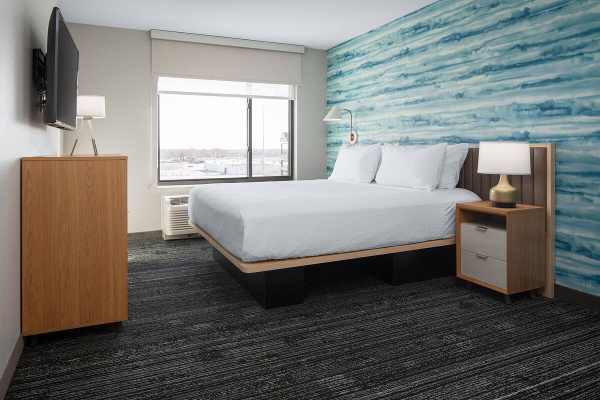 A hotel room with a bed, a TV, a desk, and a window with a view.