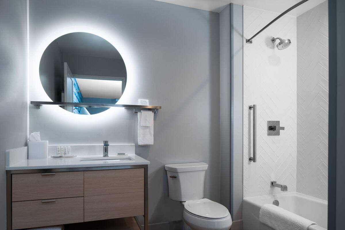 A modern bathroom with a round mirror, a toilet, a bathtub, and a shower.