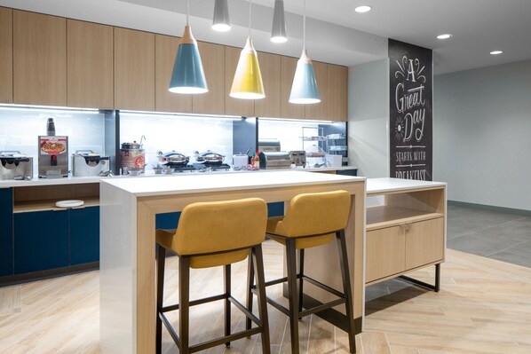 Una cocina moderna con una isla central, taburetes de bar, luces colgantes y una pared con una frase motivacional.
