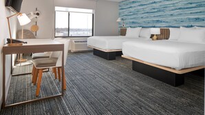 A hotel room with a desk, two beds, a large window, and a blue textured wall. - TownePlace Suites by Marriott Sidney (Sidney)