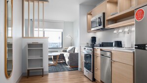 A modern kitchen with wooden cabinets, stainless steel appliances, and a dining area with a sofa and table. - TownePlace Suites by Marriott Sidney (Sidney)