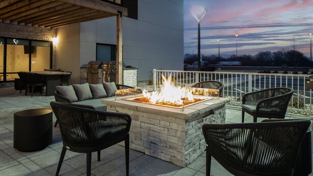 An outdoor patio with a stone fire table, black wicker chairs, and a view of the city skyline at dusk. - TownePlace Suites by Marriott Sidney (Sidney)