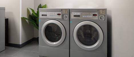 Two front-loading washing machines in a laundry room with a sign above them and a potted plant to the left.