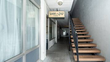 Un pasillo con una escalera que lleva a un piso superior, un letrero de 'Wash and Dry Laundry Co.' y una cámara de seguridad en el techo.