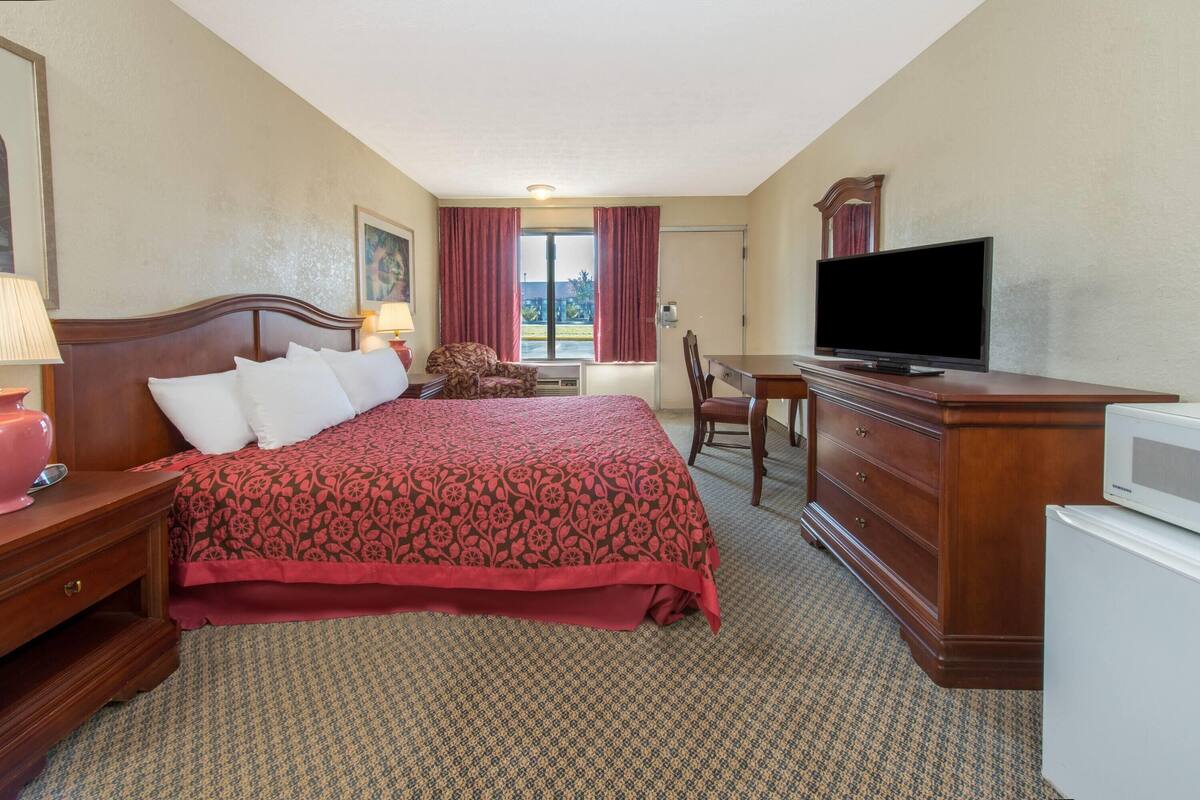 A hotel room with a bed, a television, a desk, and a refrigerator.