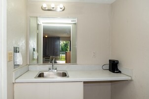 Una kitchenette pequeña con un lavamanos, un espejo y una cafetera.