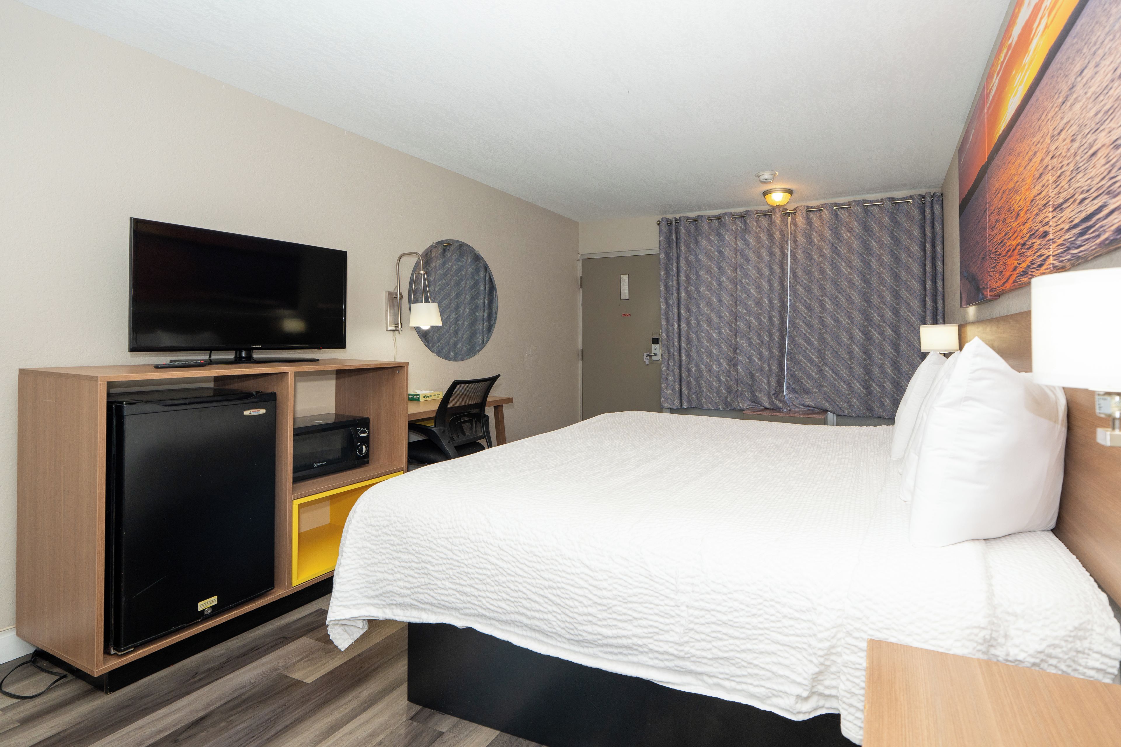 A hotel room with a bed, a television, a desk with a chair, a refrigerator, and a microwave.