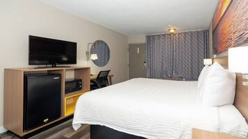 A hotel room with a bed, a television, a desk with a chair, a refrigerator, and a microwave.