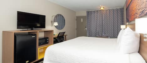 Habitación de hotel con cama, televisor, escritorio con silla, refrigerador y microondas.
