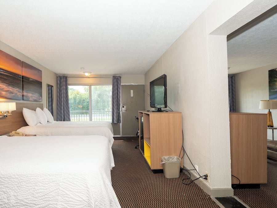 A hotel room with two beds, a television, a desk, and a painting on the wall.