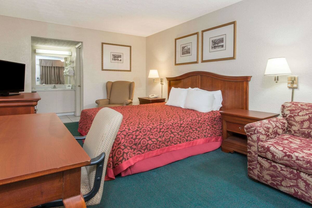 A hotel room with a bed, a desk, a chair, a sofa, a television, and framed pictures on the wall.