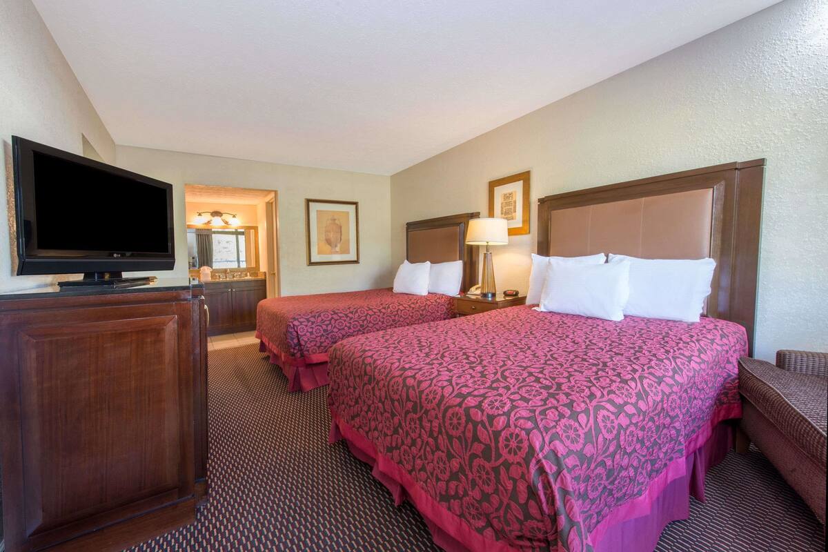 A hotel room with two beds, a television, a desk, and a mirror.