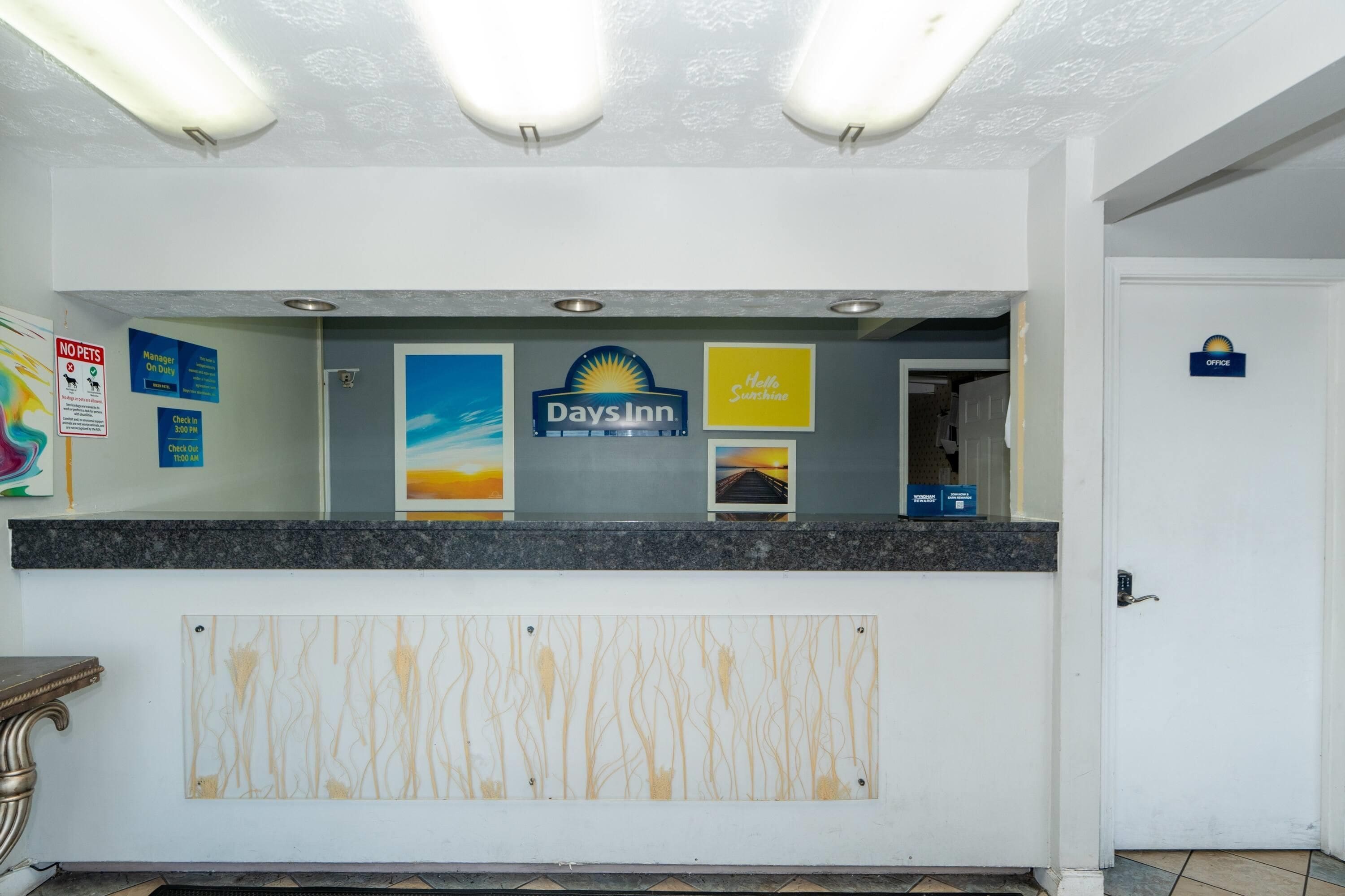A reception desk with a 'Days Inn' sign, a 'Manager On Duty' sign, a 'No Pets Allowed' sign, and a 'Check In' sign.
