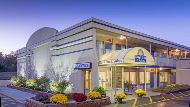 A Days Inn & Suites building with an office sign, a covered entrance, and a parking lot with flower beds. - Days Inn & Suites by Wyndham Dayton North (Dayton)