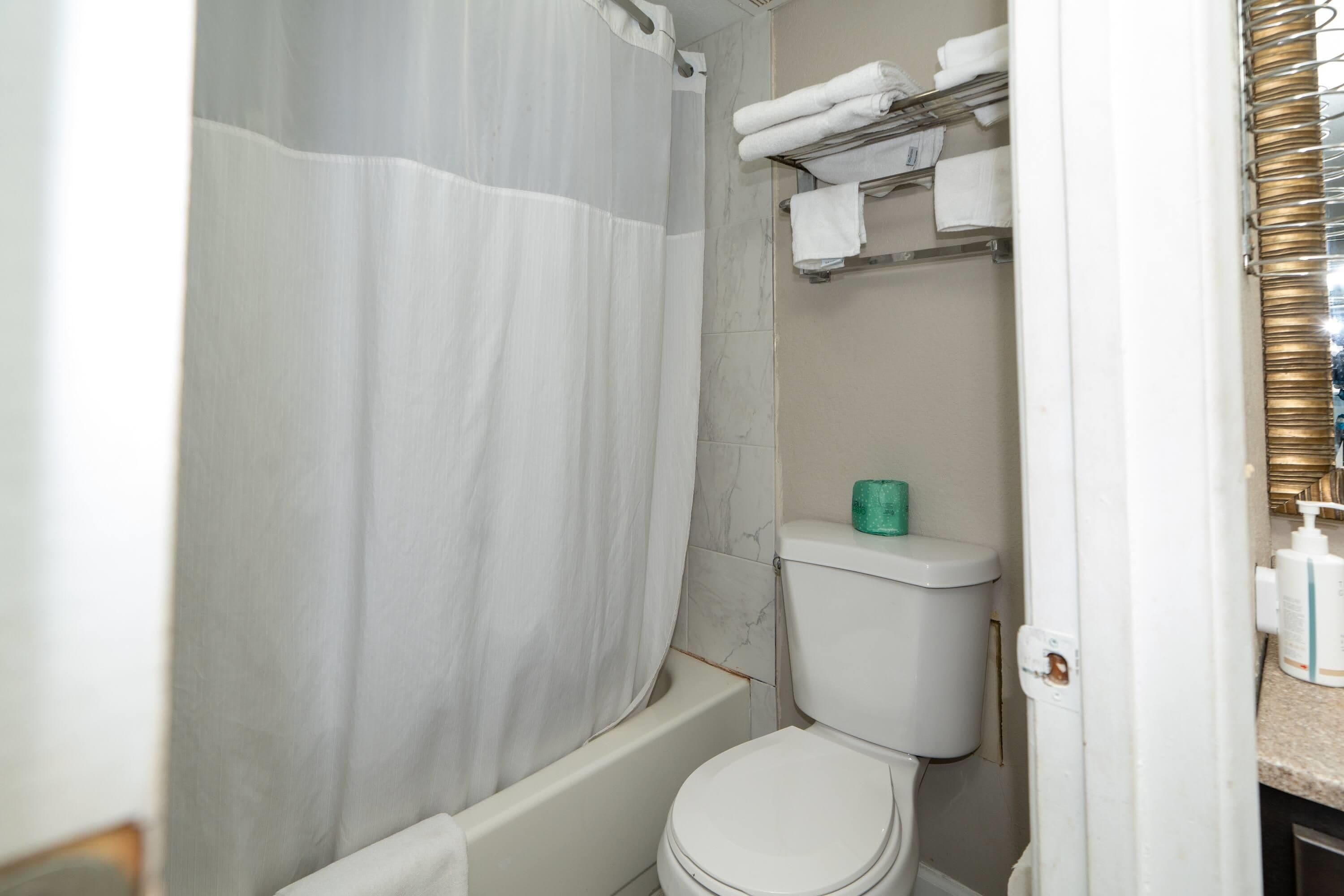 A bathroom with a shower curtain, a toilet, and a towel rack with folded towels.