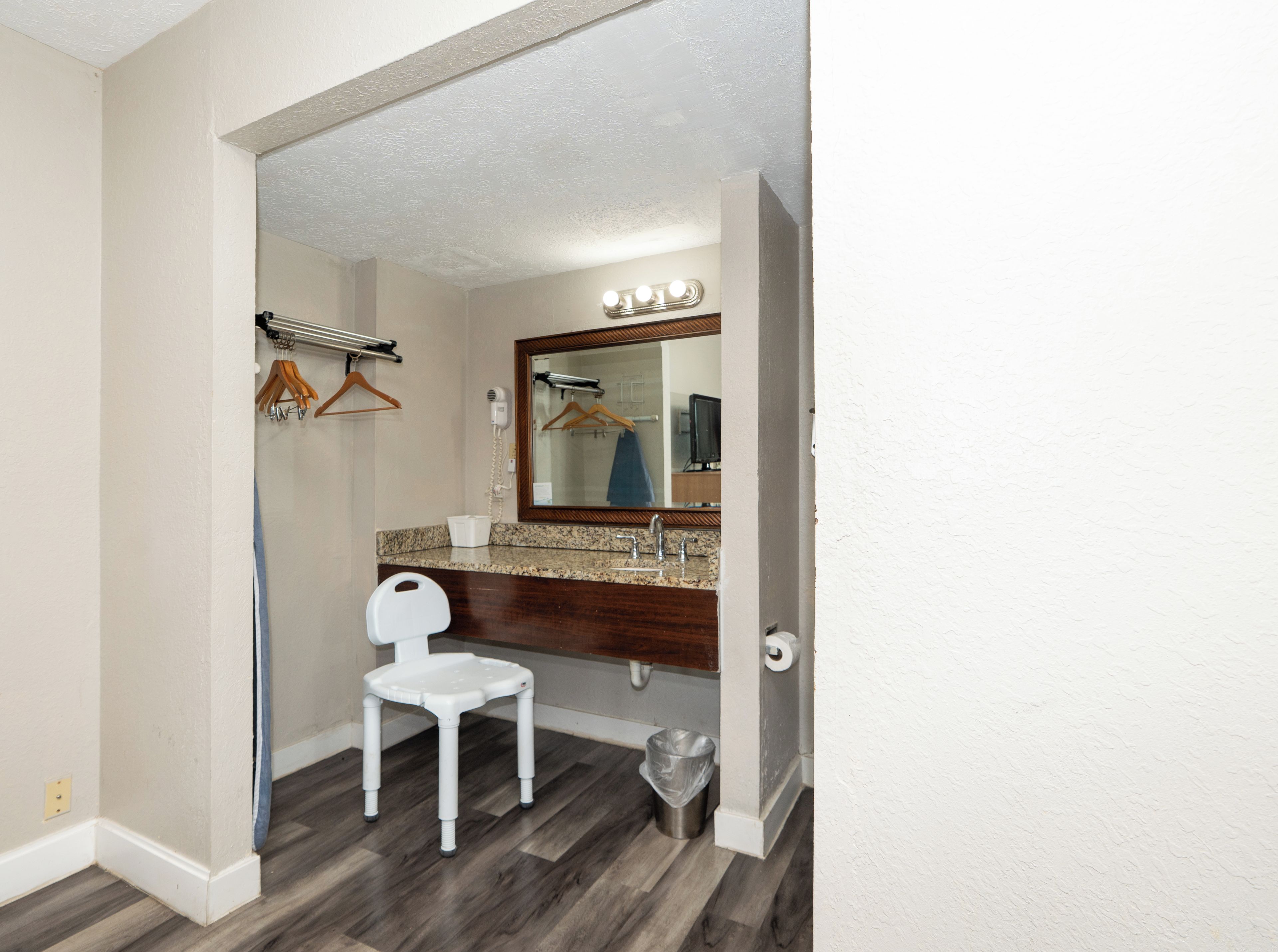 A bathroom with a vanity, a mirror, a hairdryer, a towel rack, and a trash bin.