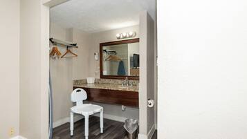 A bathroom with a vanity, a mirror, a hairdryer, a towel rack, and a trash bin.