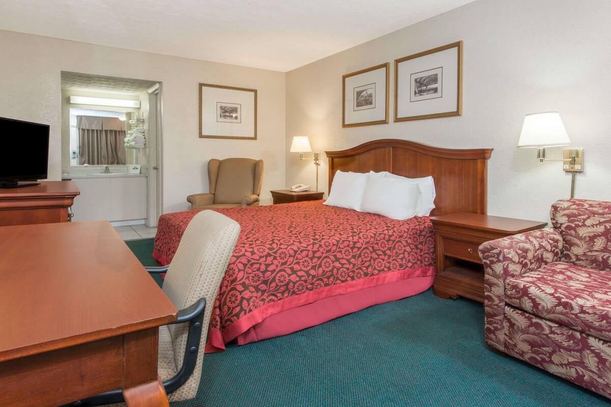 A hotel room with a bed, a desk, a chair, a television, and two framed pictures on the wall.