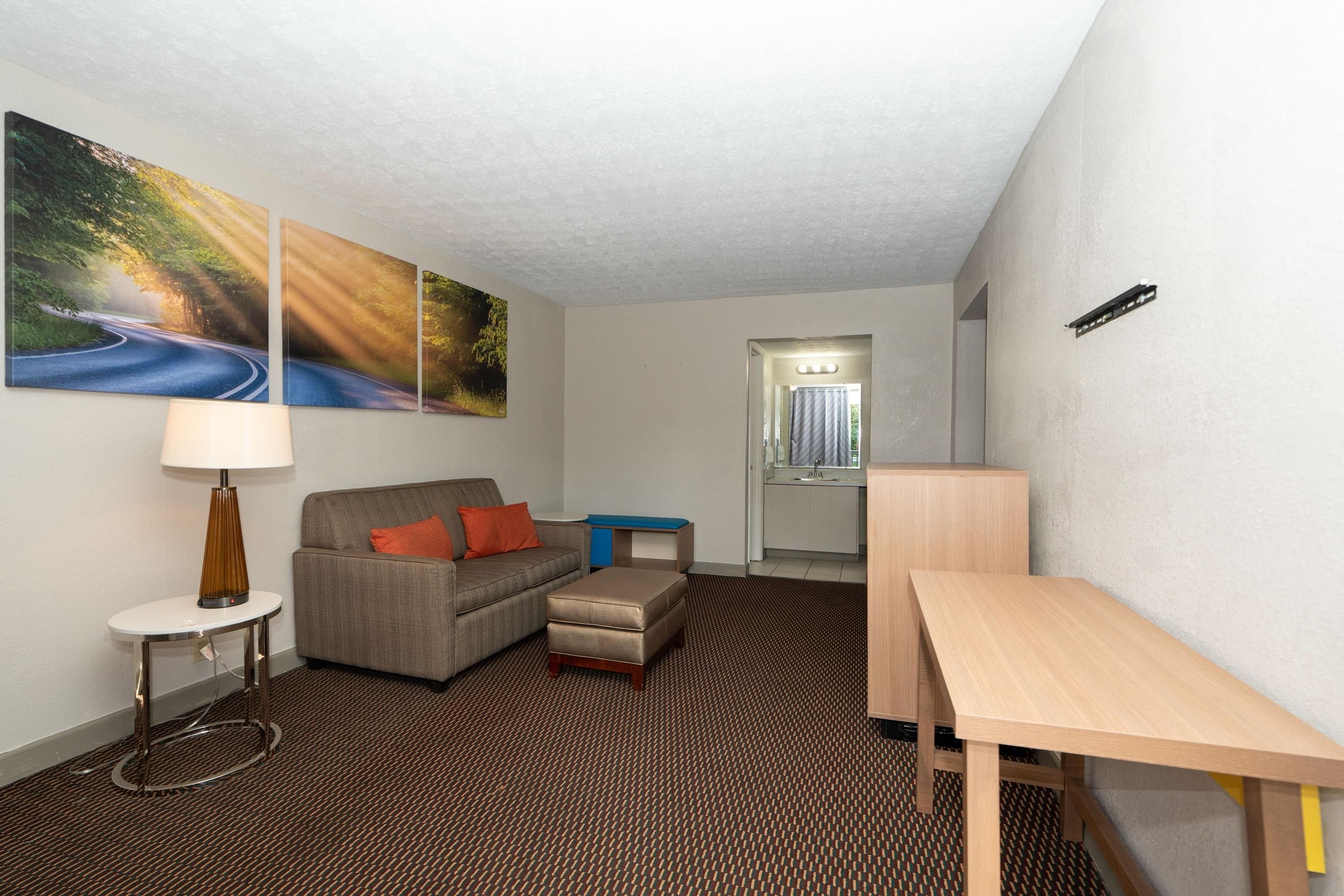 Ein Hotelzimmer mit einer Couch, einem kleinen Tisch, einer Lampe, einem Schreibtisch und einem durch eine offene Tür einsehbaren Badezimmer.