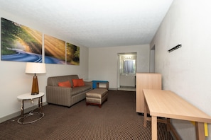 A hotel room with a sofa, a small table, a lamp, a desk, and a bathroom visible through an open door. - Days Inn & Suites by Wyndham Dayton North (Dayton)