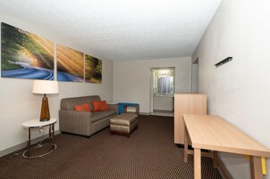 Habitación de hotel con sofá, una mesita, lámpara, escritorio y baño visible a través de una puerta abierta.