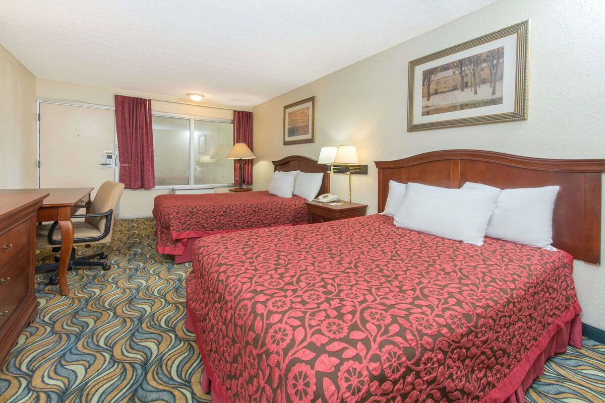 A hotel room with two beds, a desk, a chair, and a window with curtains.