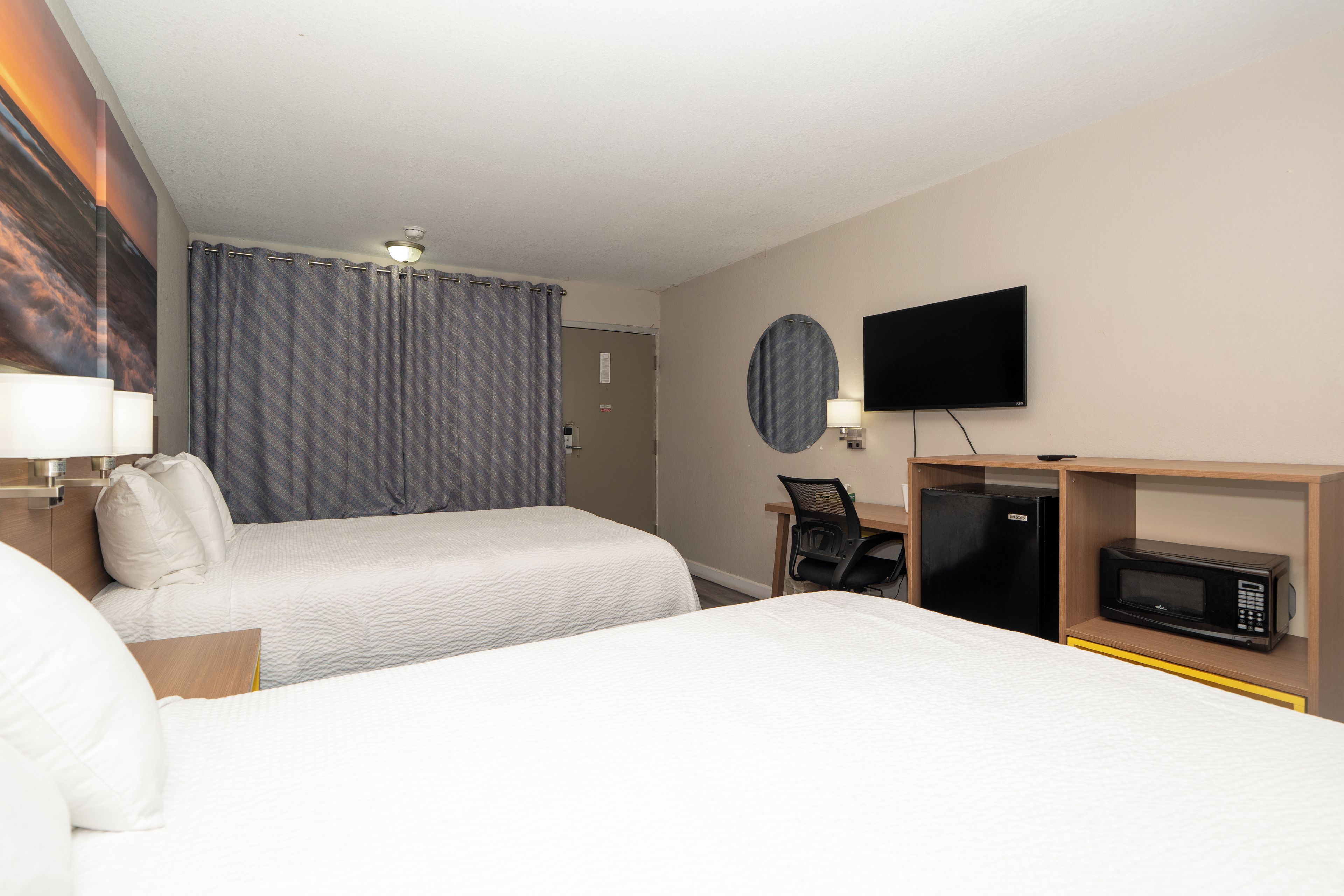 A hotel room with two beds, a television, a microwave, and a desk with a chair.