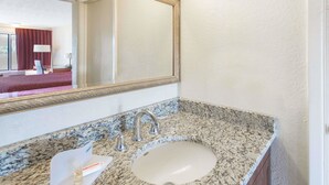 A bathroom with a granite countertop, a sink, a mirror, and a towel rack. - Days Inn & Suites by Wyndham Dayton North (Dayton)