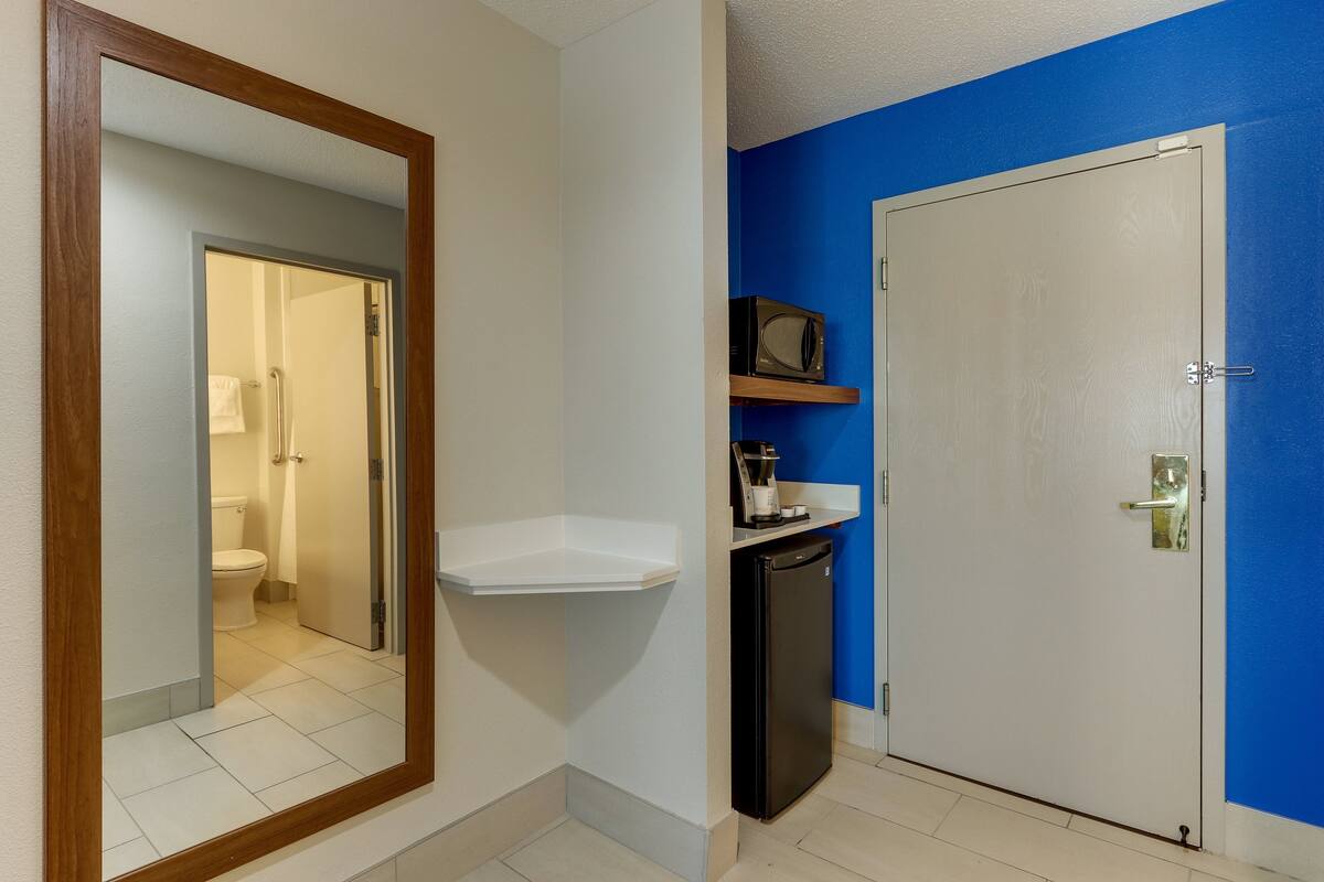 A bathroom with a white sink, a mirror, a black refrigerator, and a white door with a blue wall.