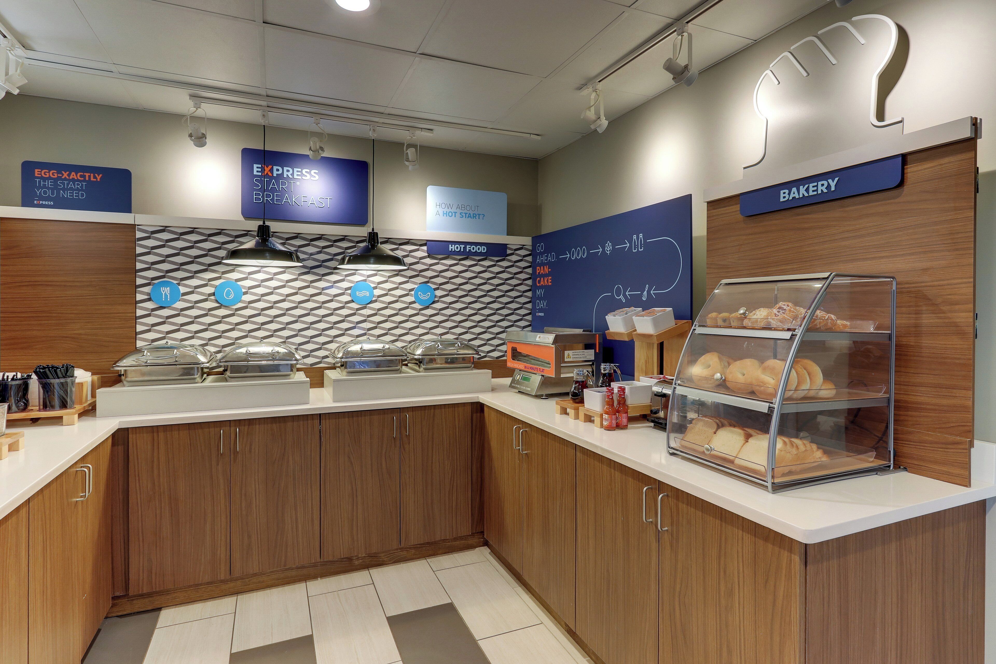A modern breakfast area with a bakery section, a counter with food service equipment, and a wall with informational signs.