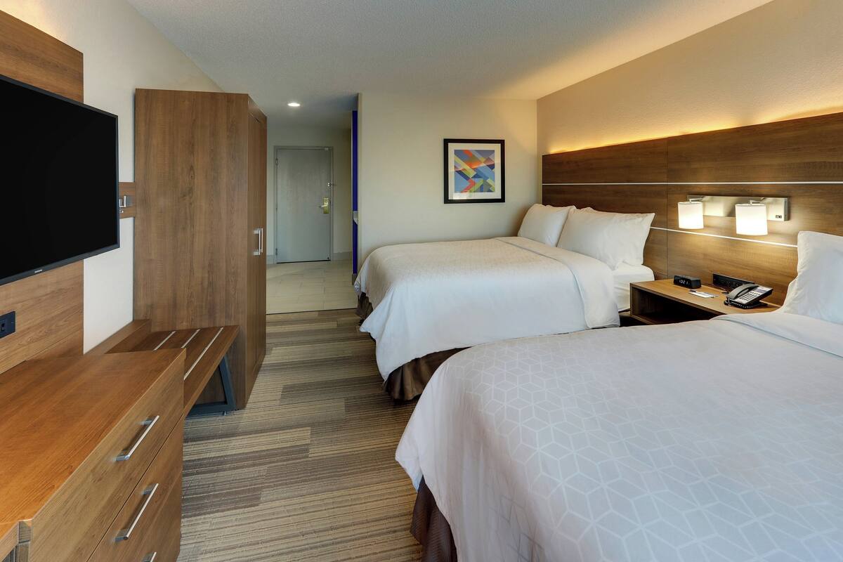 A hotel room with two beds, a TV, a desk, and a phone on the nightstand.