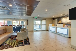 A hotel lobby with a reception desk, seating area, and a view of the outside. - Holiday Inn Express Cincinnati North - Monroe by IHG (Monroe)