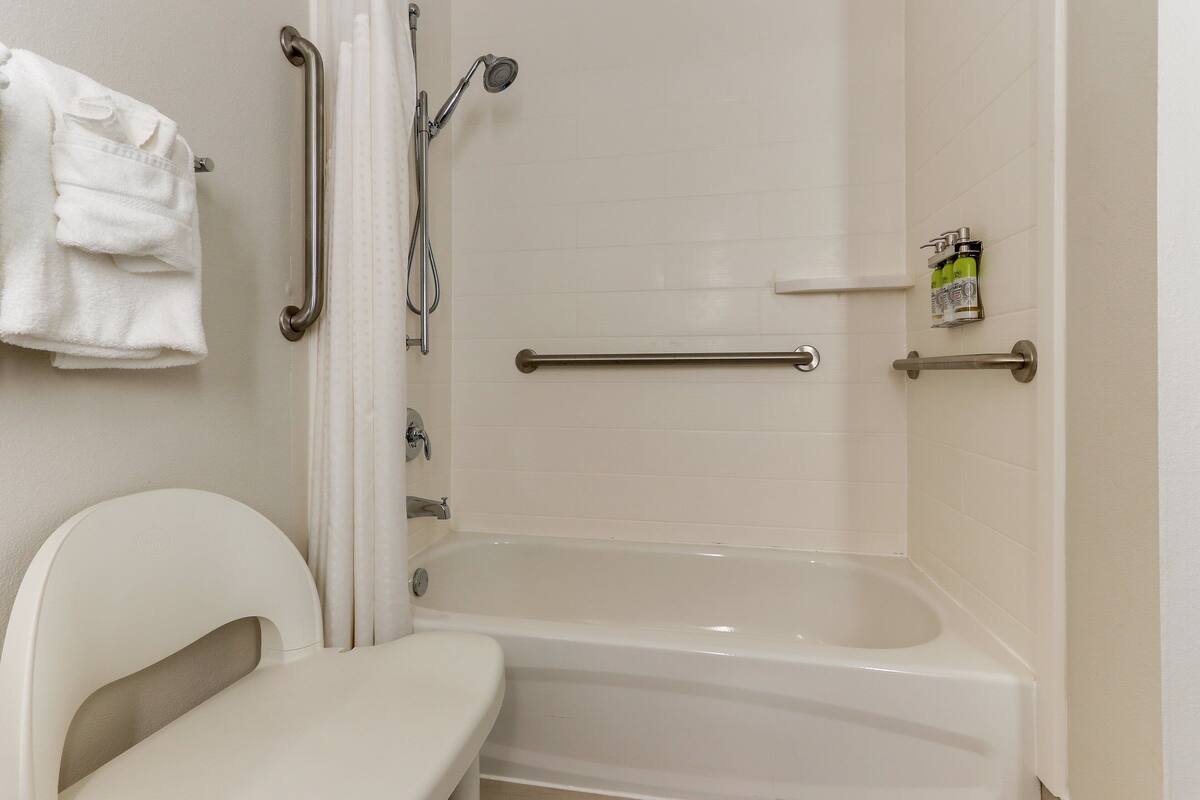 A bathroom with a bathtub, a toilet, and a shower with grab bars.