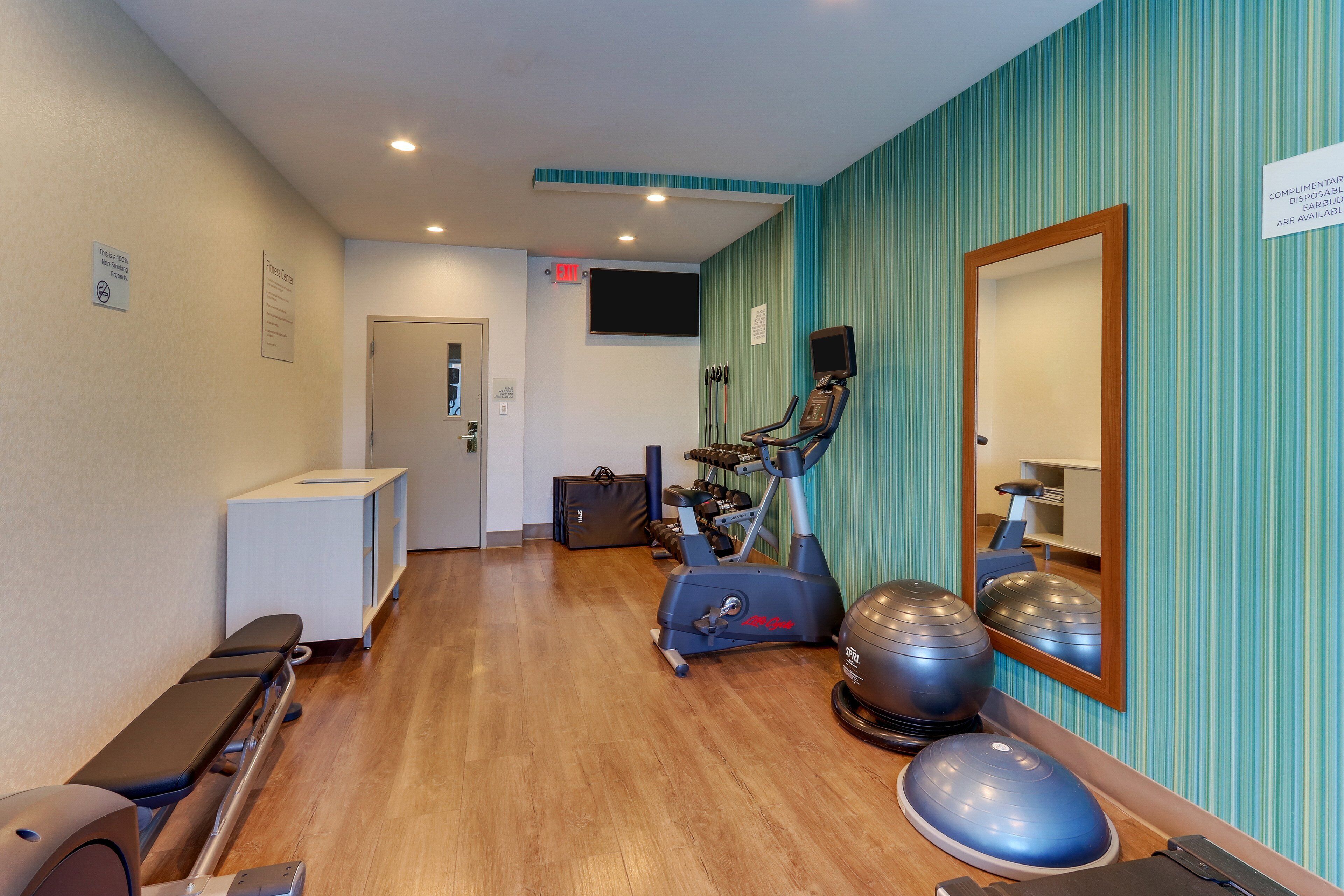 A fitness center with exercise equipment, a mirror, and a wall-mounted TV.