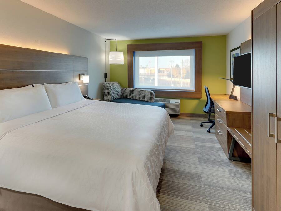 Habitación de hotel con una cama grande, un escritorio con silla, televisor y ventana con vista a edificios.