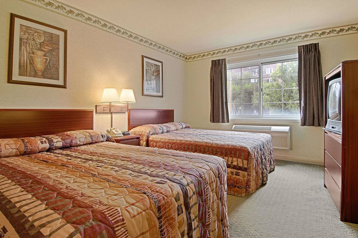 A hotel room with two beds, a TV, a lamp, and a window with curtains.