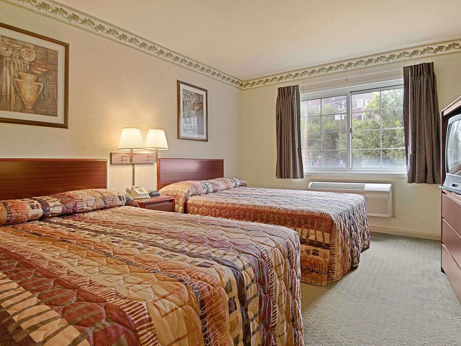 A hotel room with two beds, a TV, a lamp, and a window with curtains.